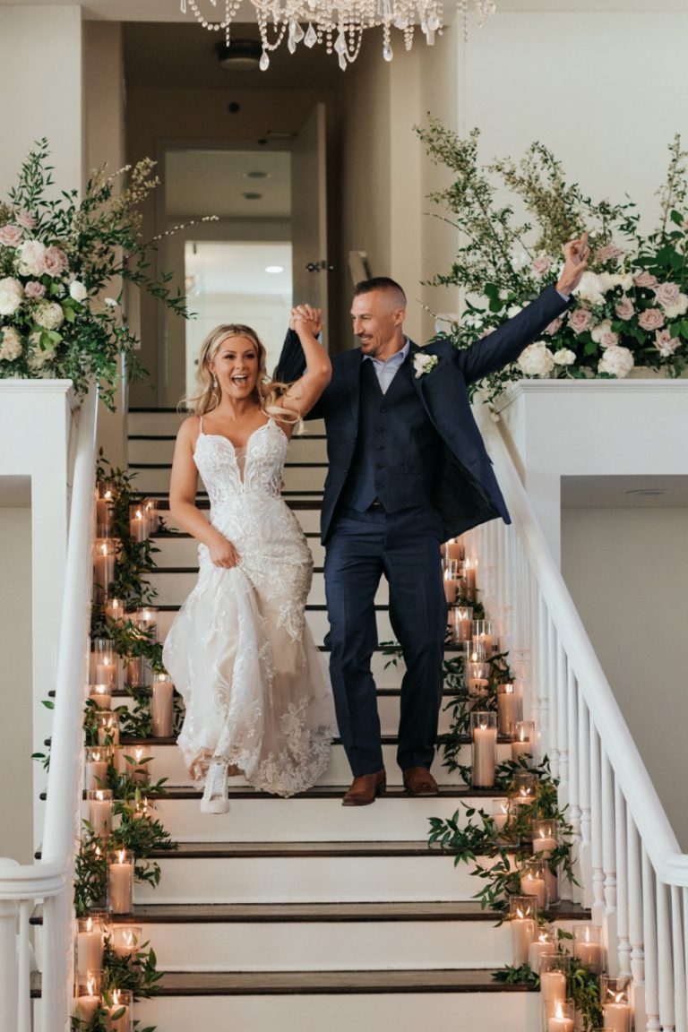 bridge and groom walking downstairs of the wedding venue with wedding floral arrangements lining the stairs