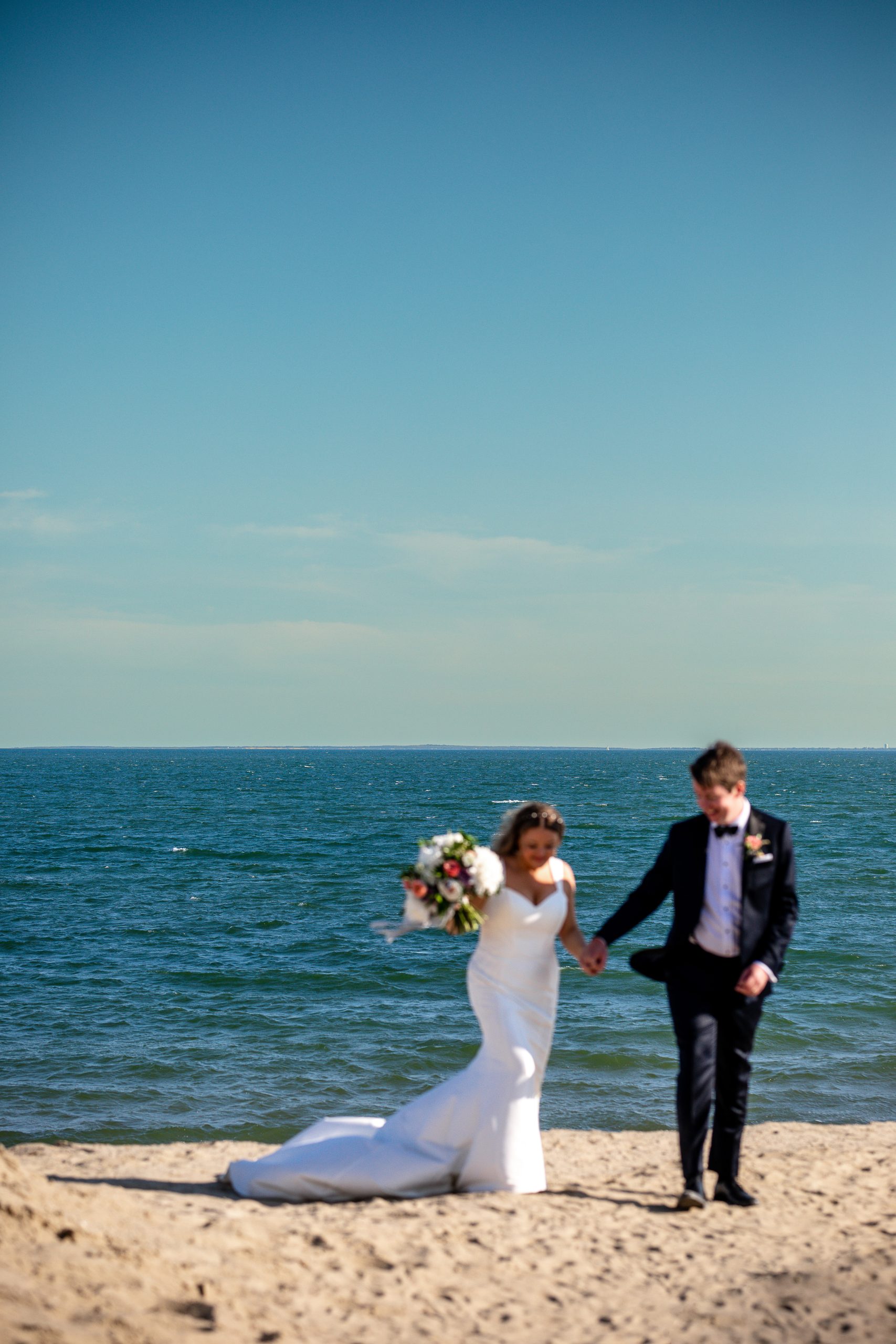 bride and groom walk on beach holding wedding bouquet